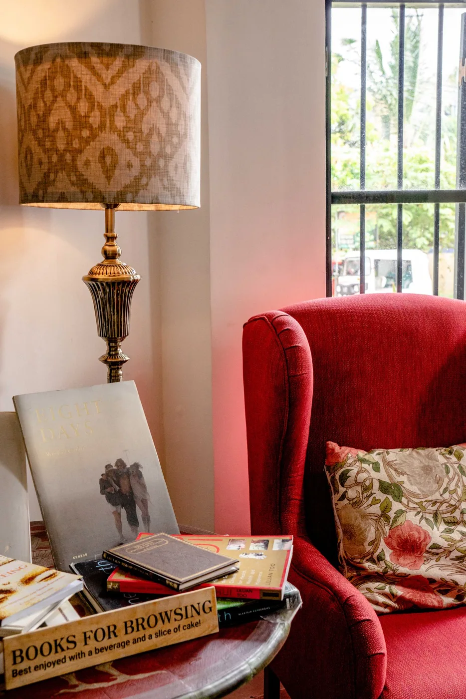 A red armchair beside a lamp and a table of books