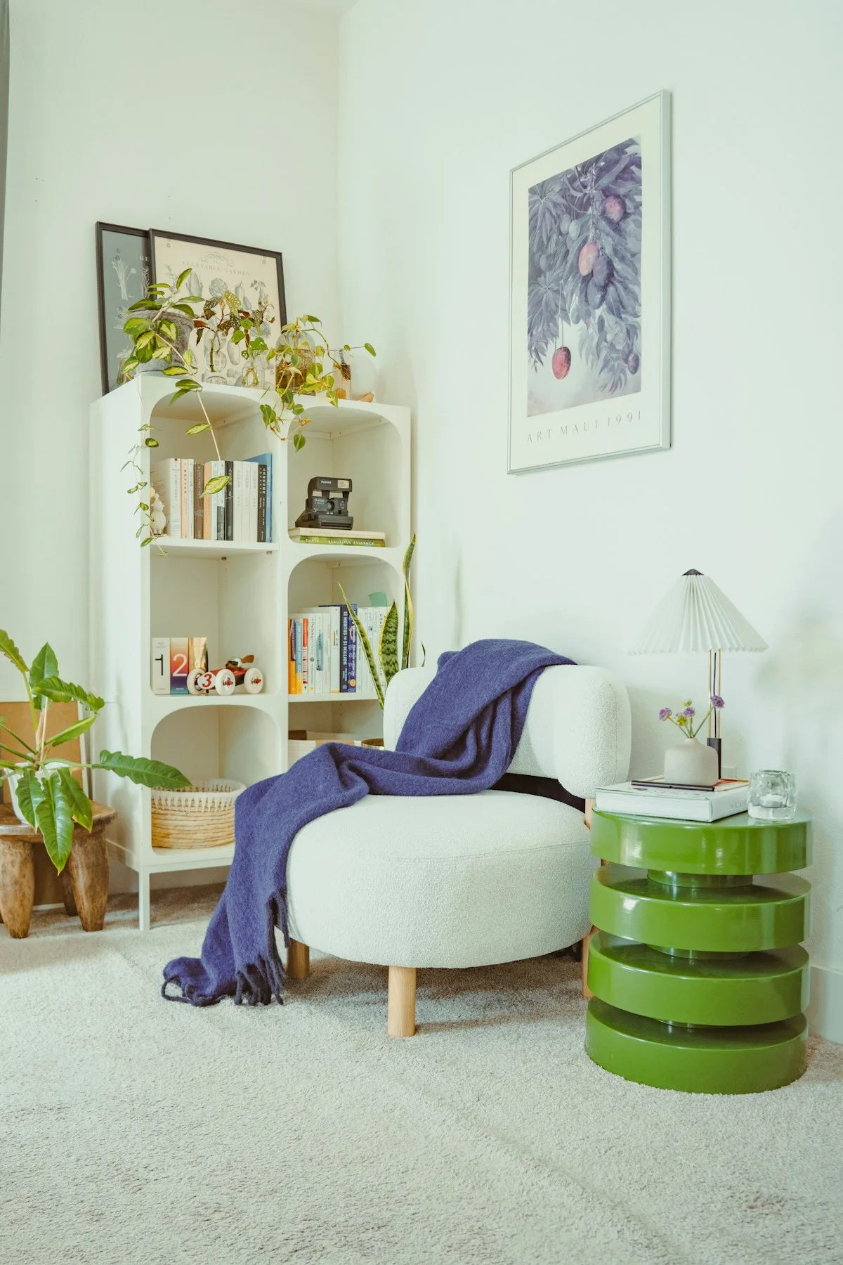 Light armchair with a blue throw, round green side table and bookshelves