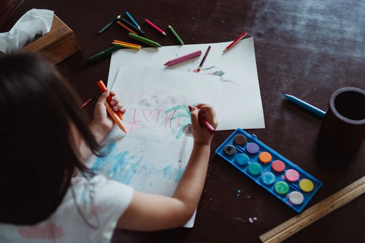 Child drawing on paper with crayons and a watercolor set