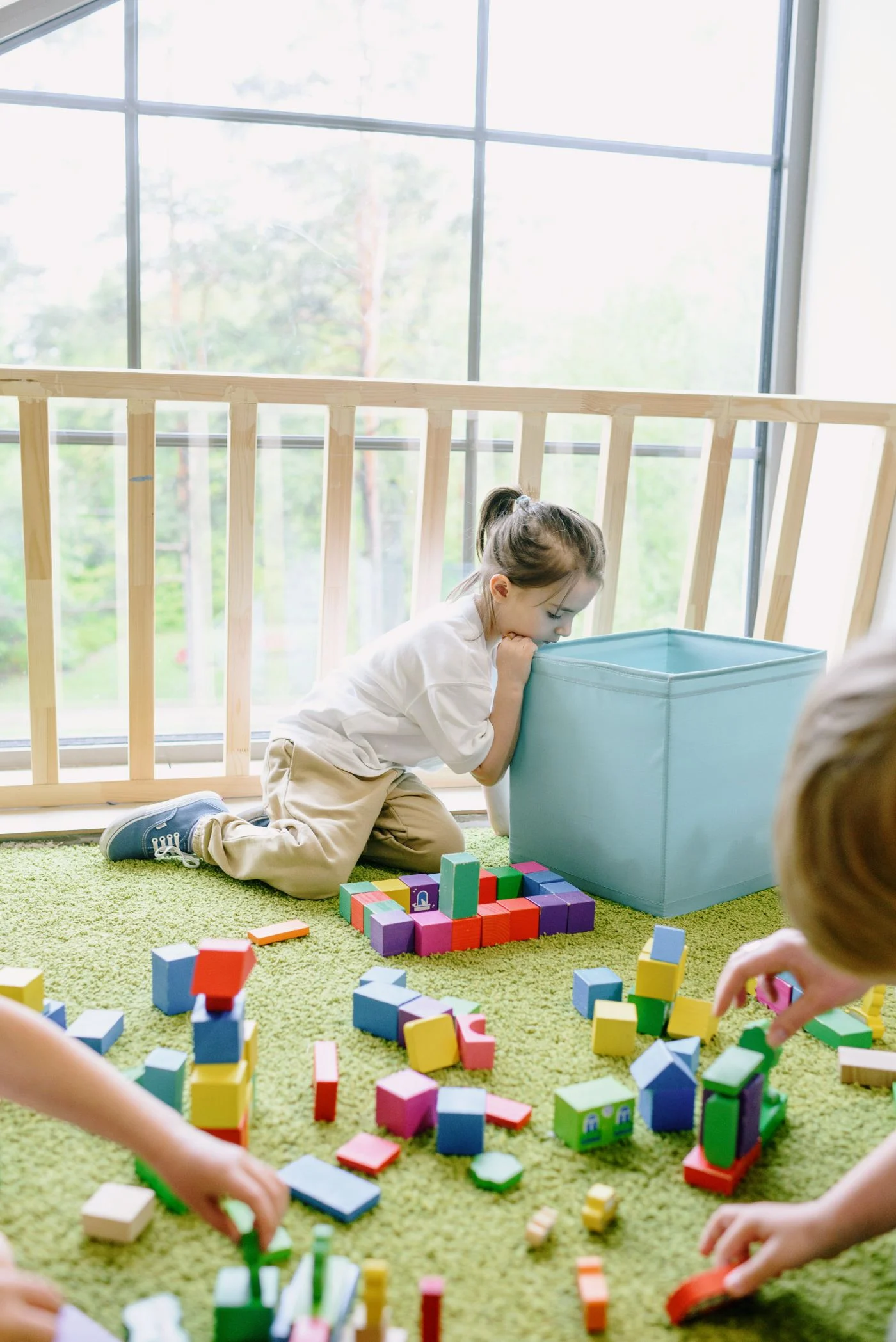 Child beside a blue storage bin and colorful blocks on the floor