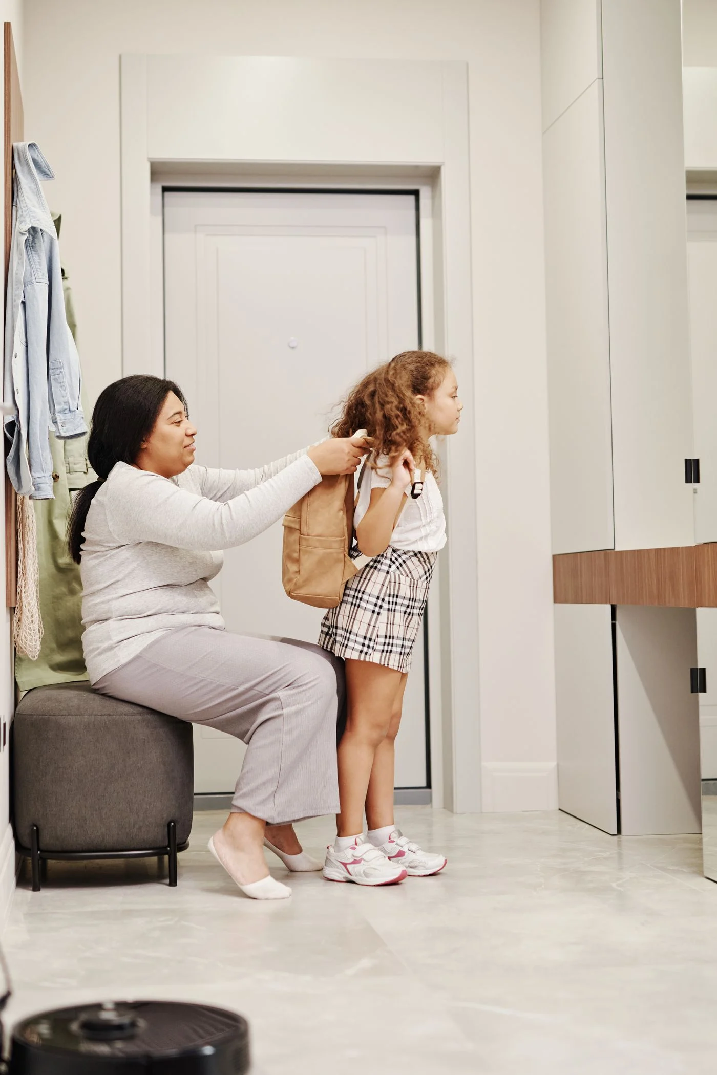 Mother helping a child put on a backpack indoors