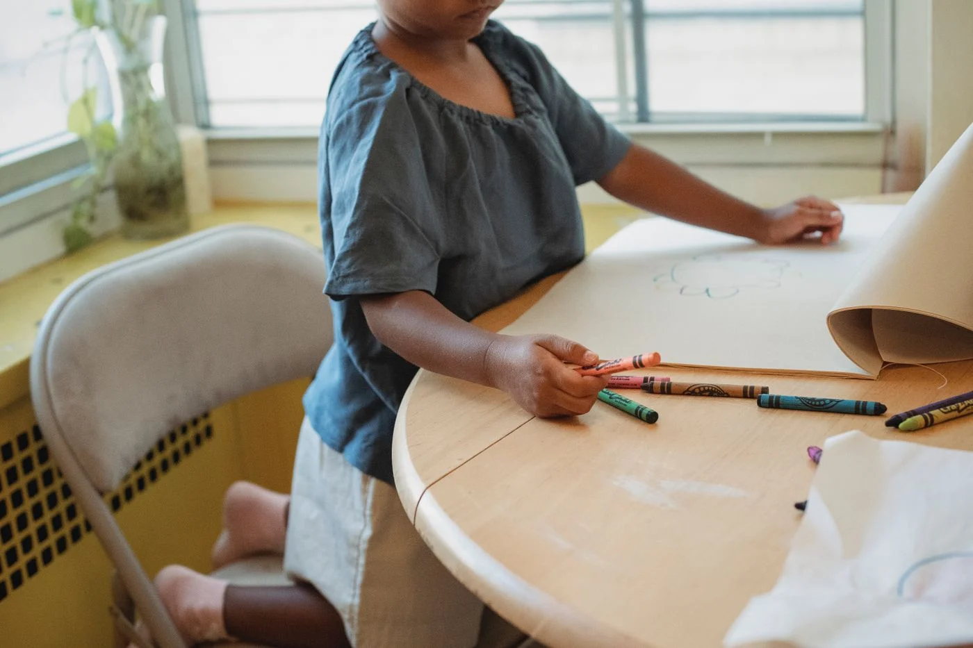 Child seated at a table drawing with crayons on paper