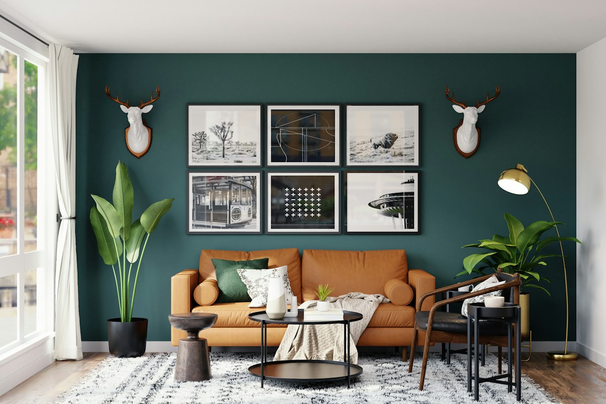 A tan sofa and plants against a dark green wall with framed pictures