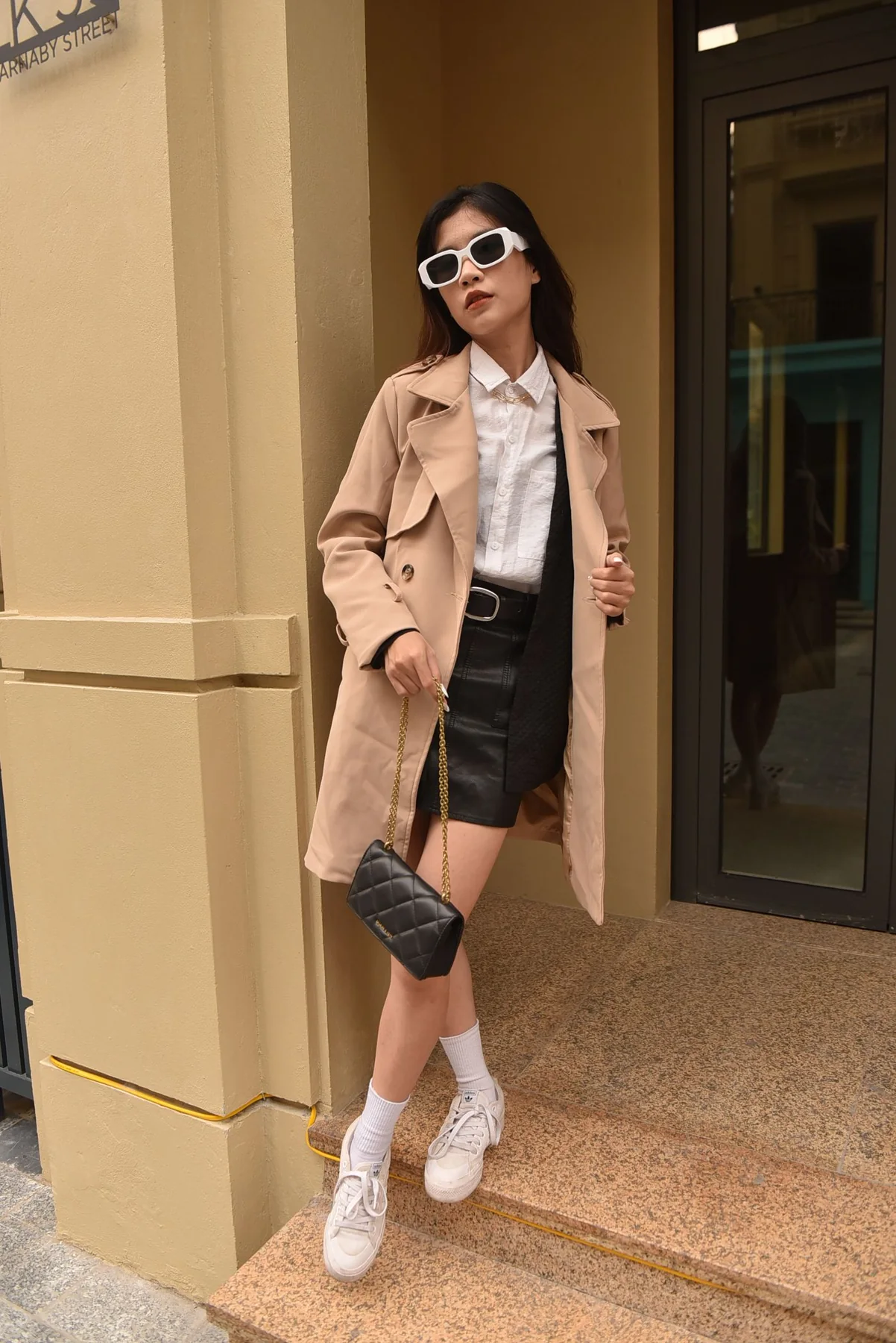 A woman wearing a beige coat over a pale shirt and dark shorts